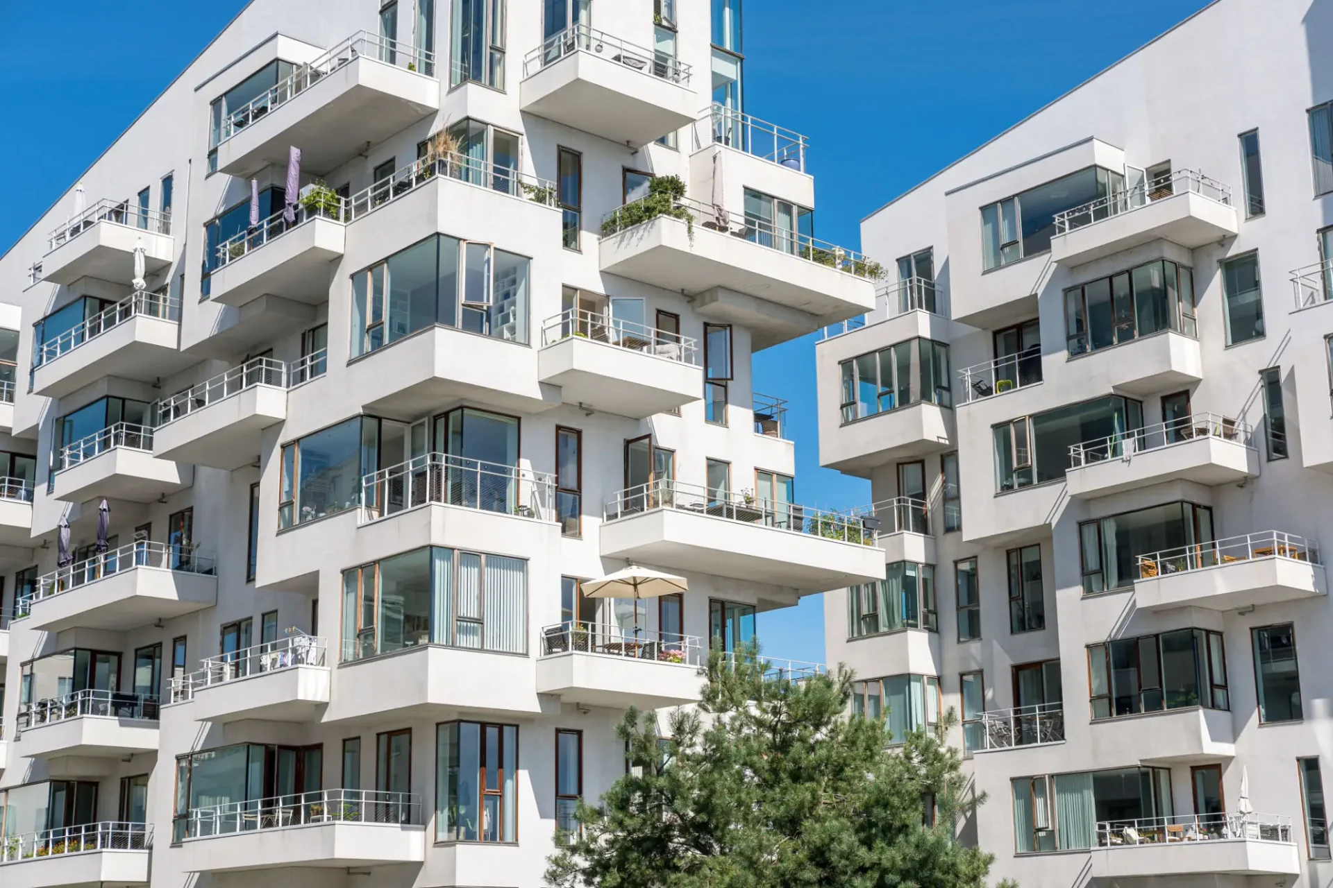 Modern white apartment buildings with balconies under a clear blue sky.