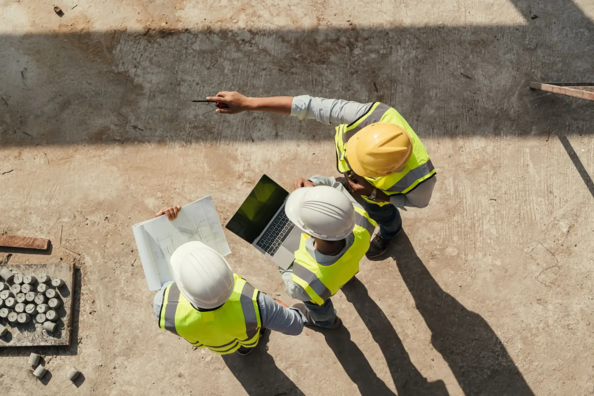 Two construction workers in helmets and vests reviewing a blueprint outdoors.