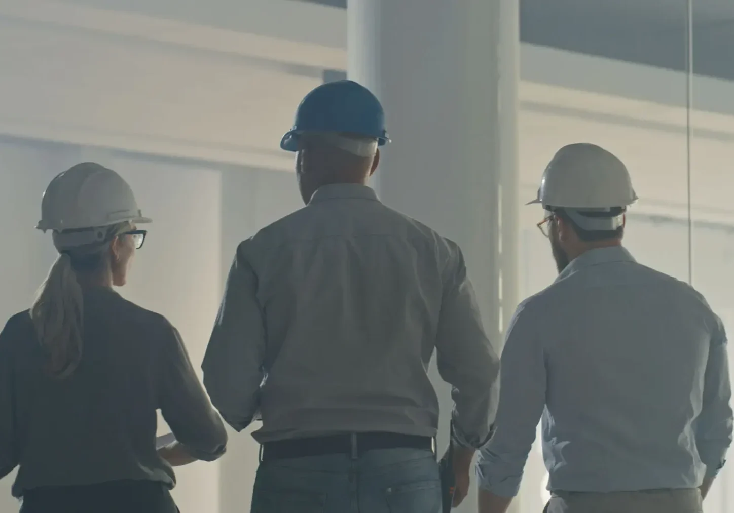 Three construction workers wearing helmets and safety gear at a building site.